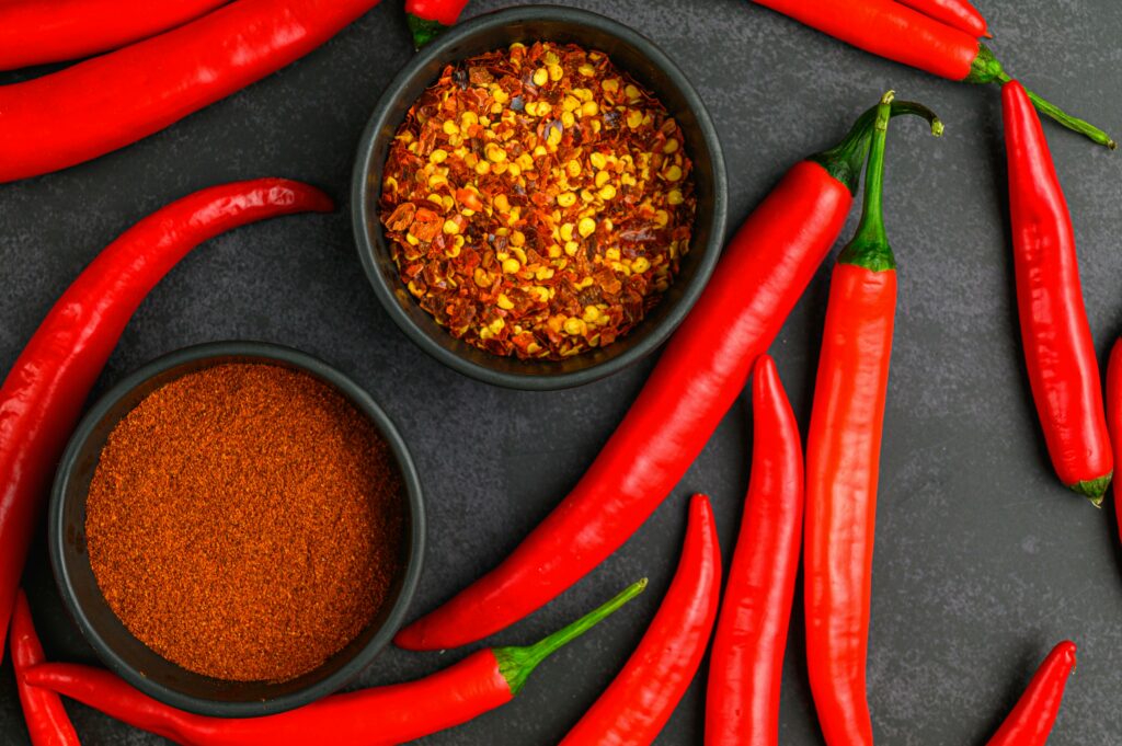 dried cayenne pepper flakes in a bowl with fresh cayenne 